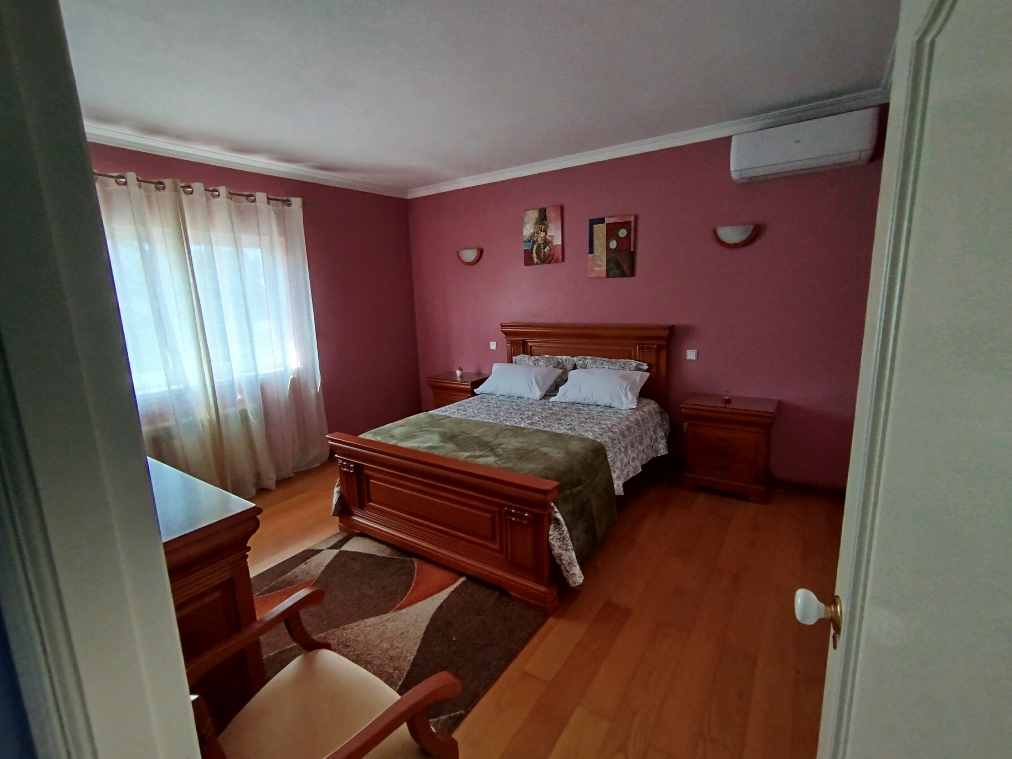 A bedroom with a wooden bed, a nightstand, a chair, and a window with curtains.
