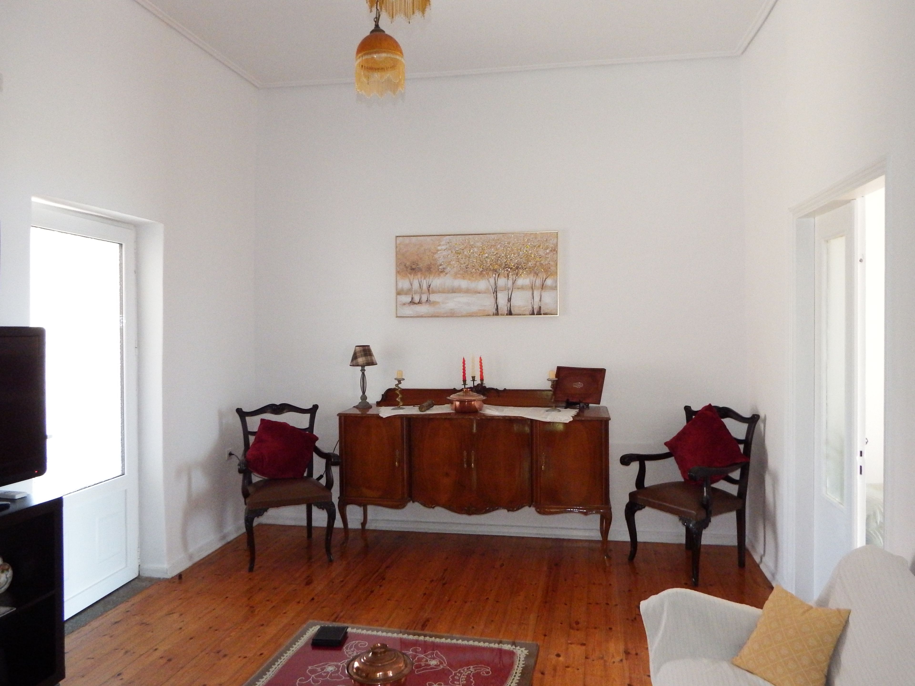 A living room with a wooden floor, a sofa, two armchairs, a cabinet, a painting, and a television.