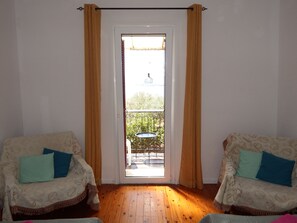 A room with two patterned armchairs, a wooden floor, a door leading to an outdoor balcony with a table and chairs. - Nandia's Molyvos House (Mithymna)