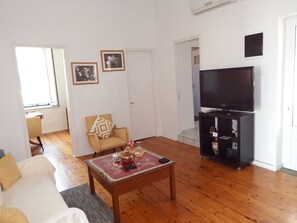 A living room with a sofa, a coffee table with decorative items, a television on a stand, and a door leading to another room.