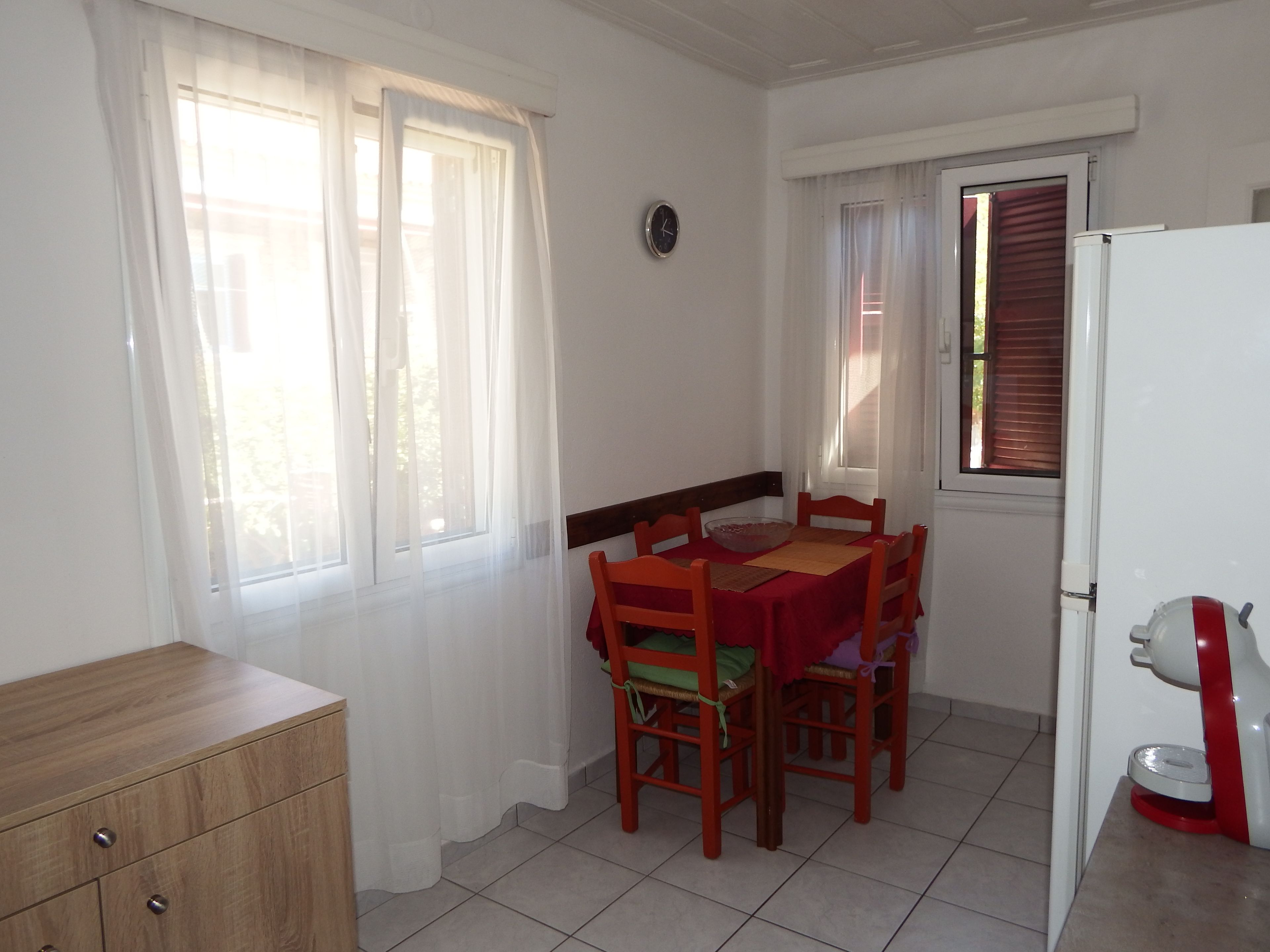 A dining area with a table and chairs, a clock on the wall, and a refrigerator.