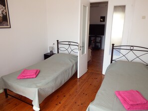 Une chambre avec deux lits simples, une table de chevet avec une lampe et un plancher en bois.