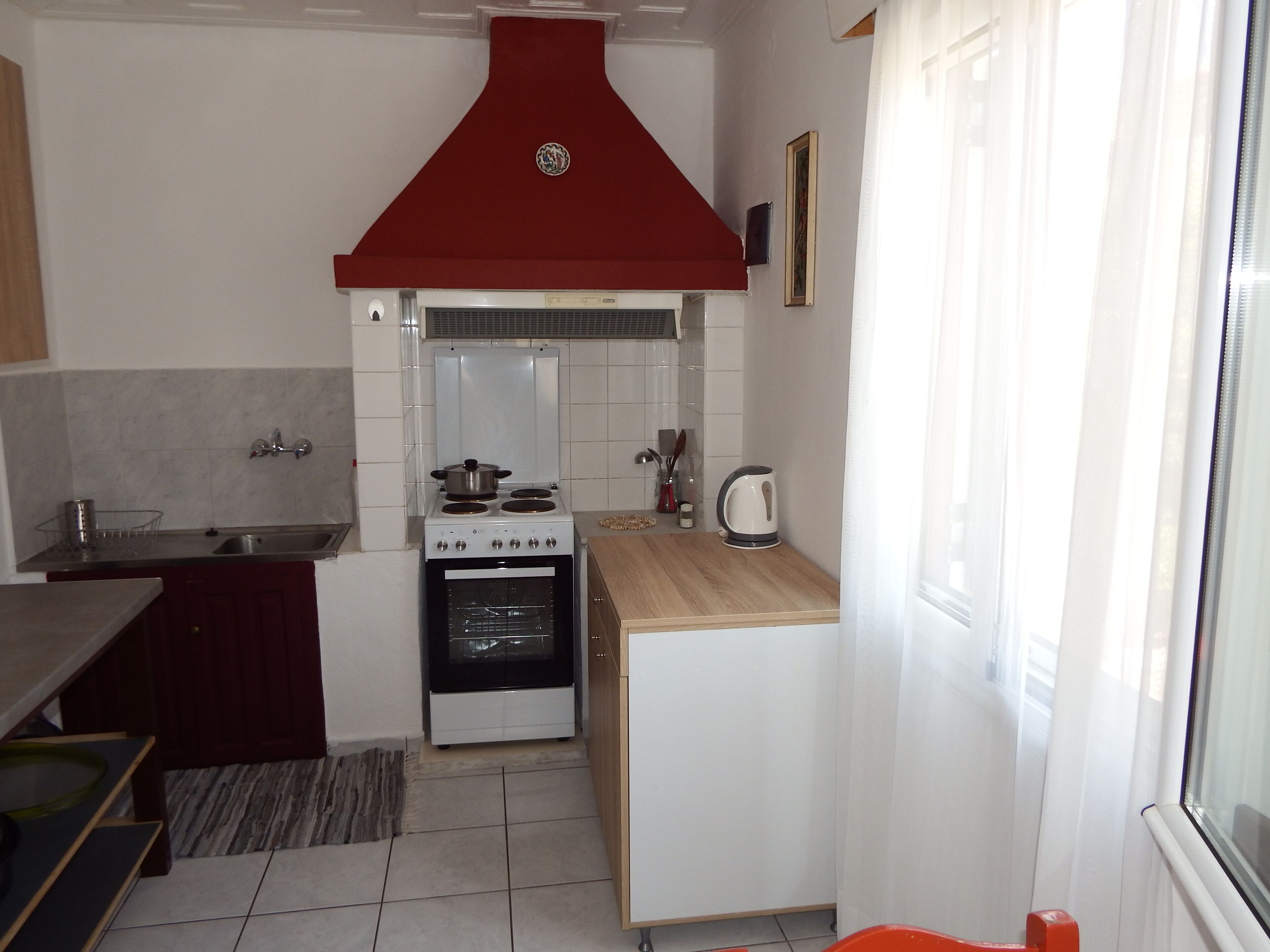 A compact kitchen with a stove, oven, and a red range hood.