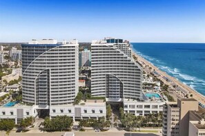 A high-rise hotel with a curved facade, a pool, and a beach view.