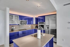 A modern kitchen with blue cabinets, stainless steel appliances, and a central island.