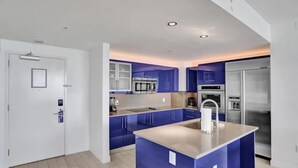 Eine moderne Küche mit blauen Schränken, einer zentralen Kochinsel, Edelstahlgeräten und Einbauleuchten.