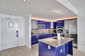 A modern kitchen with blue cabinets, a central island, stainless steel appliances, and recessed ceiling lights. - 18th Floor Luxury W Residence - 2 King Suites, Pools & 2-min walk to Beach (Fort Lauderdale)
