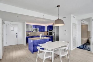 A modern kitchen with blue cabinets, a white dining table, and a pendant light.