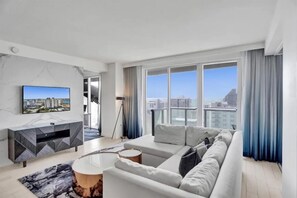 A modern living room with a large window, a flat-screen TV, a sofa, and a side table. - 18th Floor Luxury W Residence - 2 King Suites, Pools & 2-min walk to Beach (Fort Lauderdale)