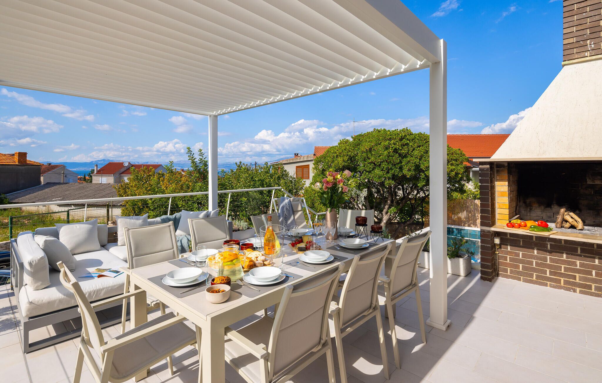 An outdoor patio with a table set for dining, surrounded by chairs, and a barbecue grill.