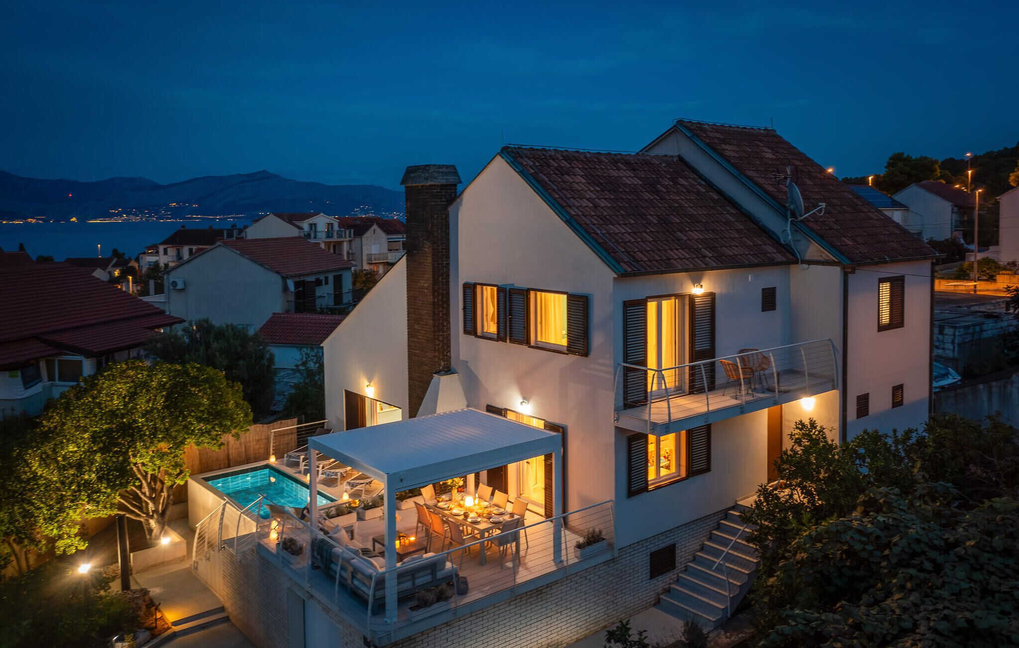 A two-story house with a swimming pool, outdoor seating, and a balcony.