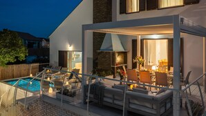 Et moderne hus med en pool, udendørs møbler og en godt oplyst patio.