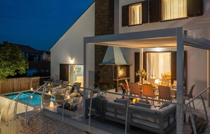 Ein modernes Haus mit Pool, Sitzgelegenheiten im Freien und einer gut beleuchteten Terrasse.