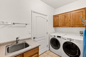 Une buanderie équipée d’un lave-linge, d’un évier, de meubles en bois et d’une porte.