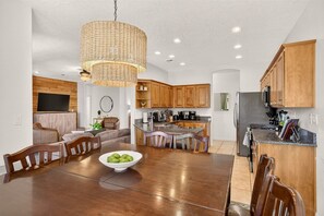 A modern kitchen with wooden cabinets, a central island, and a dining area with a wooden table and chairs. - 5BR Ivins Getaway Near Snow Canyon, UT (Ivins)
