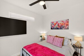 A bedroom with a bed, a ceiling fan, a wall-mounted TV, and a floral painting. - 5BR Ivins Getaway Near Snow Canyon, UT (Ivins)