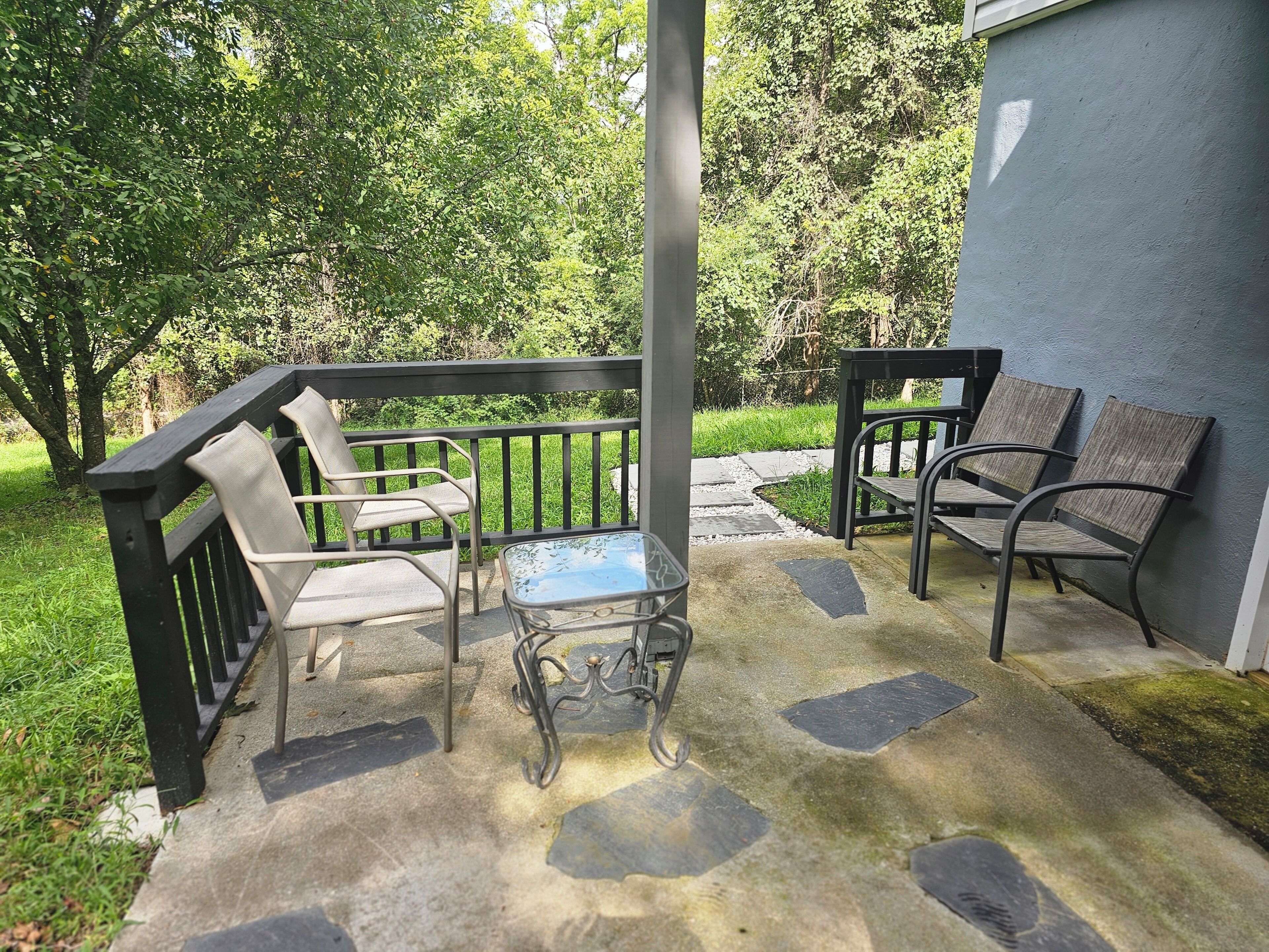 Un patio con mesa y dos sillas, una mesita de cristal y un sendero de piedra que lleva a una zona con césped.