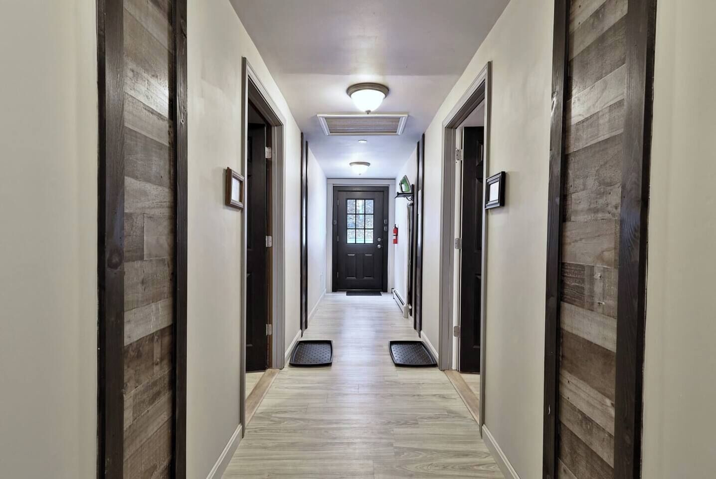 Un couloir d’hôtel avec un sol de couleur claire, des portes en bois foncé et une porte noire au bout.