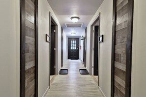 Un pasillo de hotel con piso de color claro, puertas de madera oscura y una puerta negra al final.