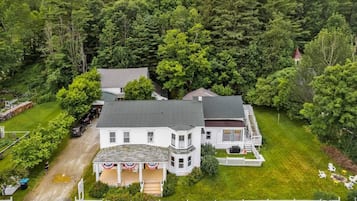 Une maison à deux étages avec un porche, entourée d’une pelouse bien entretenue et d’arbres touffus.