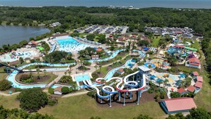 Ein Luftbild eines Wasserparks mit mehreren Wasserrutschen und Becken, umgeben von Parkplätzen und Grünflächen.