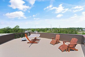 Une terrasse sur le toit avec un hamac, deux fauteuils Adirondack et une vue sur un paysage verdoyant.