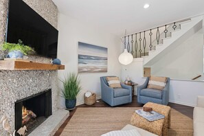 A modern living room with a fireplace, two armchairs, a large painting, and a staircase. - The Gilded Egret at Massengale  Beach (St. Simons Island)