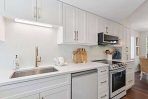 A modern kitchen with white cabinetry, stainless steel appliances, and a built-in oven. - The Gilded Egret at Massengale  Beach (St. Simons Island)