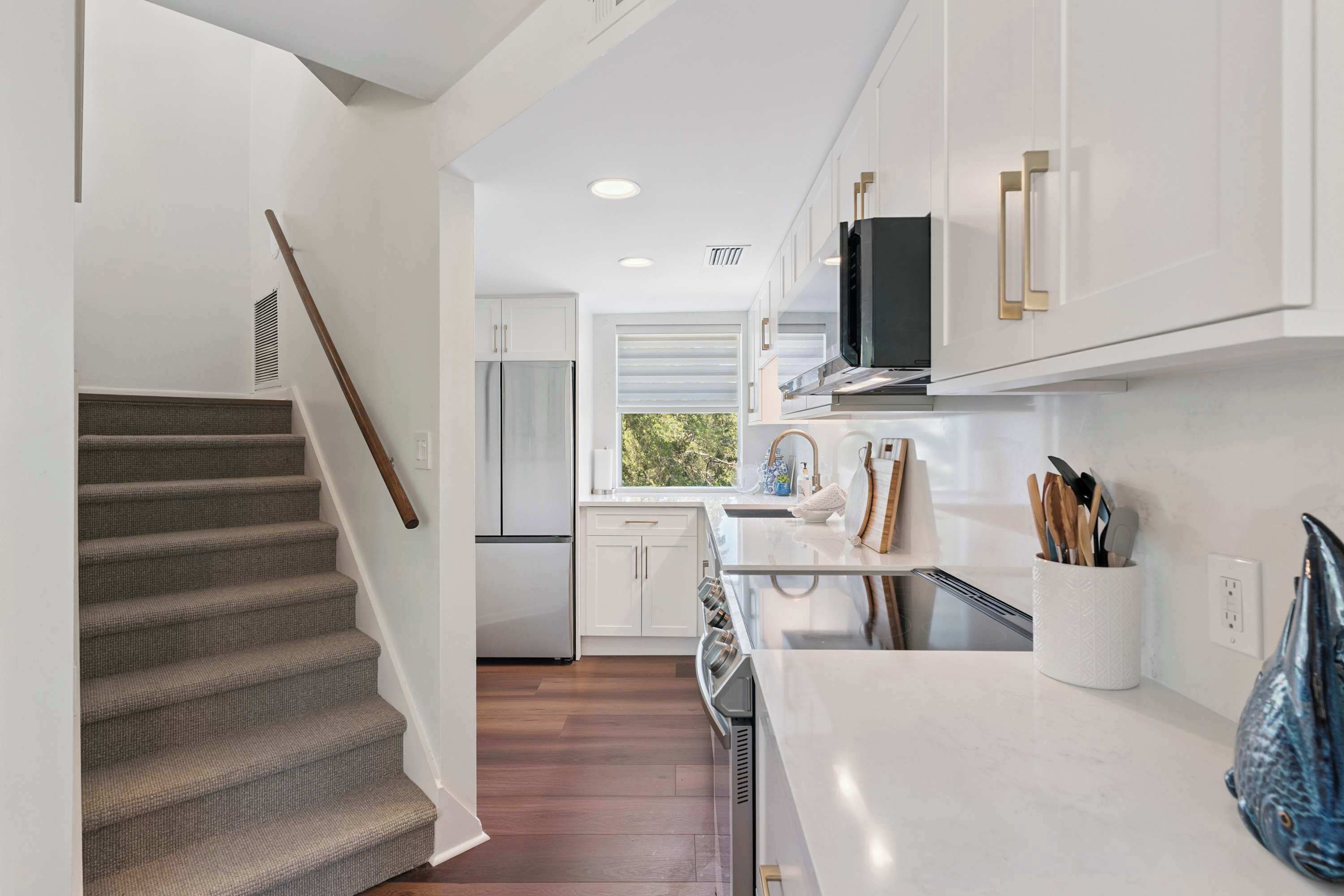 A modern kitchen with white cabinetry, a stainless steel refrigerator, and a window providing natural light.