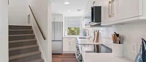 A modern kitchen with white cabinetry, a stainless steel refrigerator, and a window providing natural light.