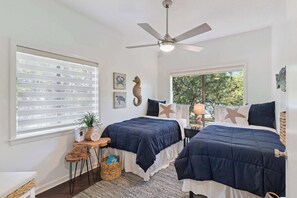 A bedroom with two beds, a ceiling fan, and a large window. - The Gilded Egret at Massengale  Beach (St. Simons Island)