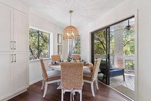 A dining area with a round table, wicker chairs, and a hanging light fixture. - The Gilded Egret at Massengale  Beach (St. Simons Island)