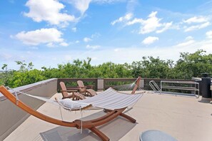 A rooftop terrace with a hammock, wooden chairs, and a metal railing. - The Gilded Egret at Massengale  Beach (St. Simons Island)