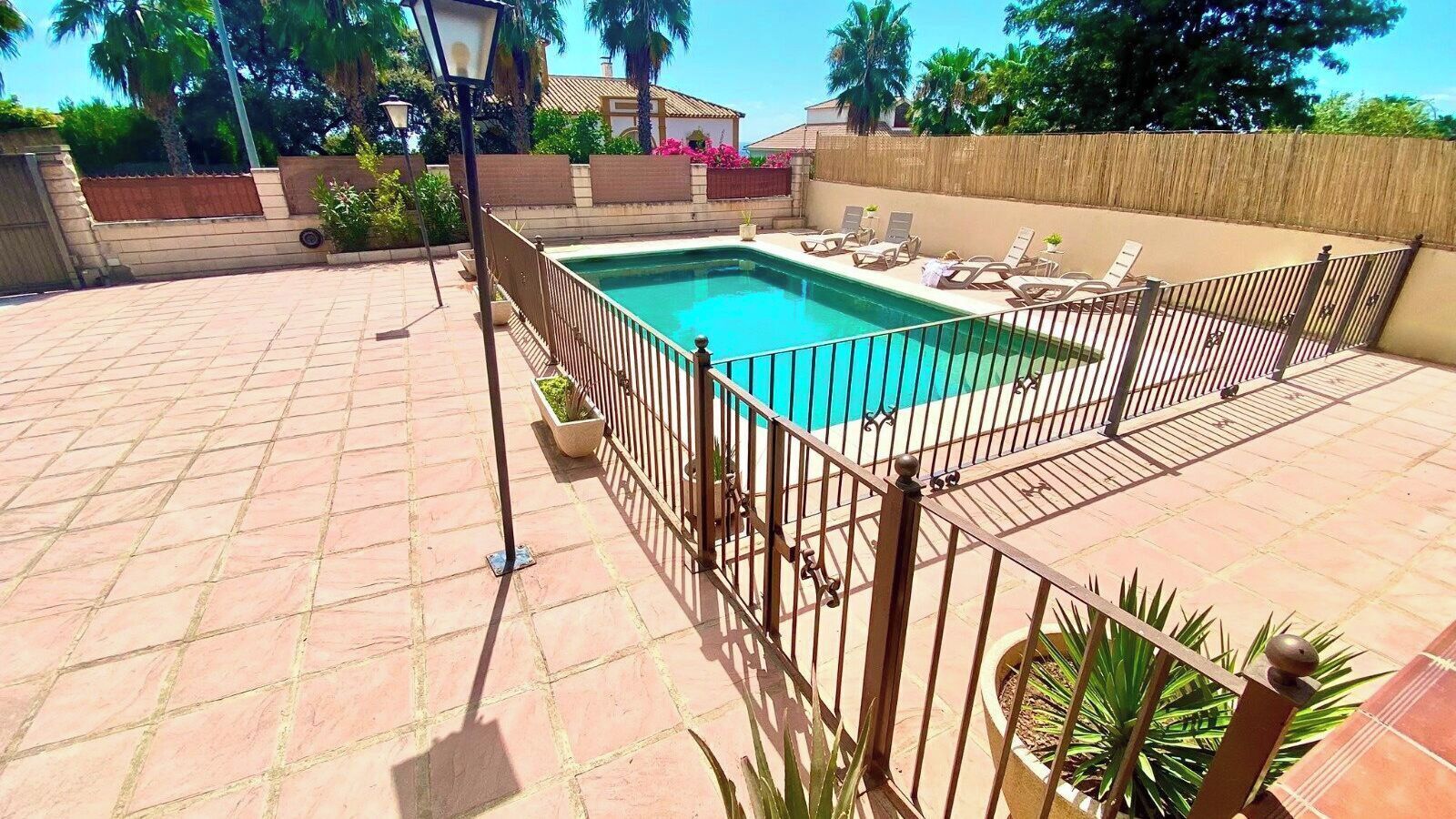 Una piscina rectangular con valla metálica, rodeada por un patio empedrado.