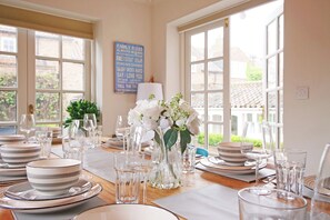 A dining table set for a meal with clear glassware and plates, a vase with white flowers, and a 'Family Rules' sign on the wall.
