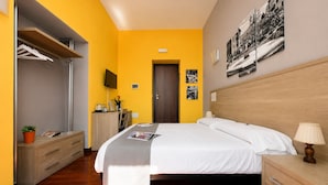 A hotel room with a bed, bedside table, lamp, and a desk with a chair.