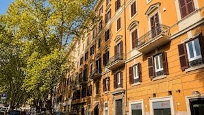 A row of multi-story buildings with balconies, a clear sky, and a tree with green leaves.
