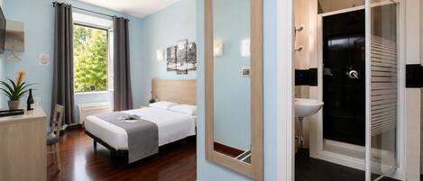 Een hotelkamer met een bed, nachtkastje, een spiegel, een douche en uitzicht op groen.