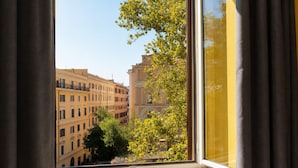 A window with a view of a building with multiple stories and balconies, a tree with green leaves, and a clear sky.