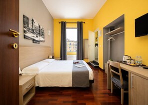 A hotel room with a bed, bedside table, desk, chair, and a view of the city. - The Guesthouse (Rome)
