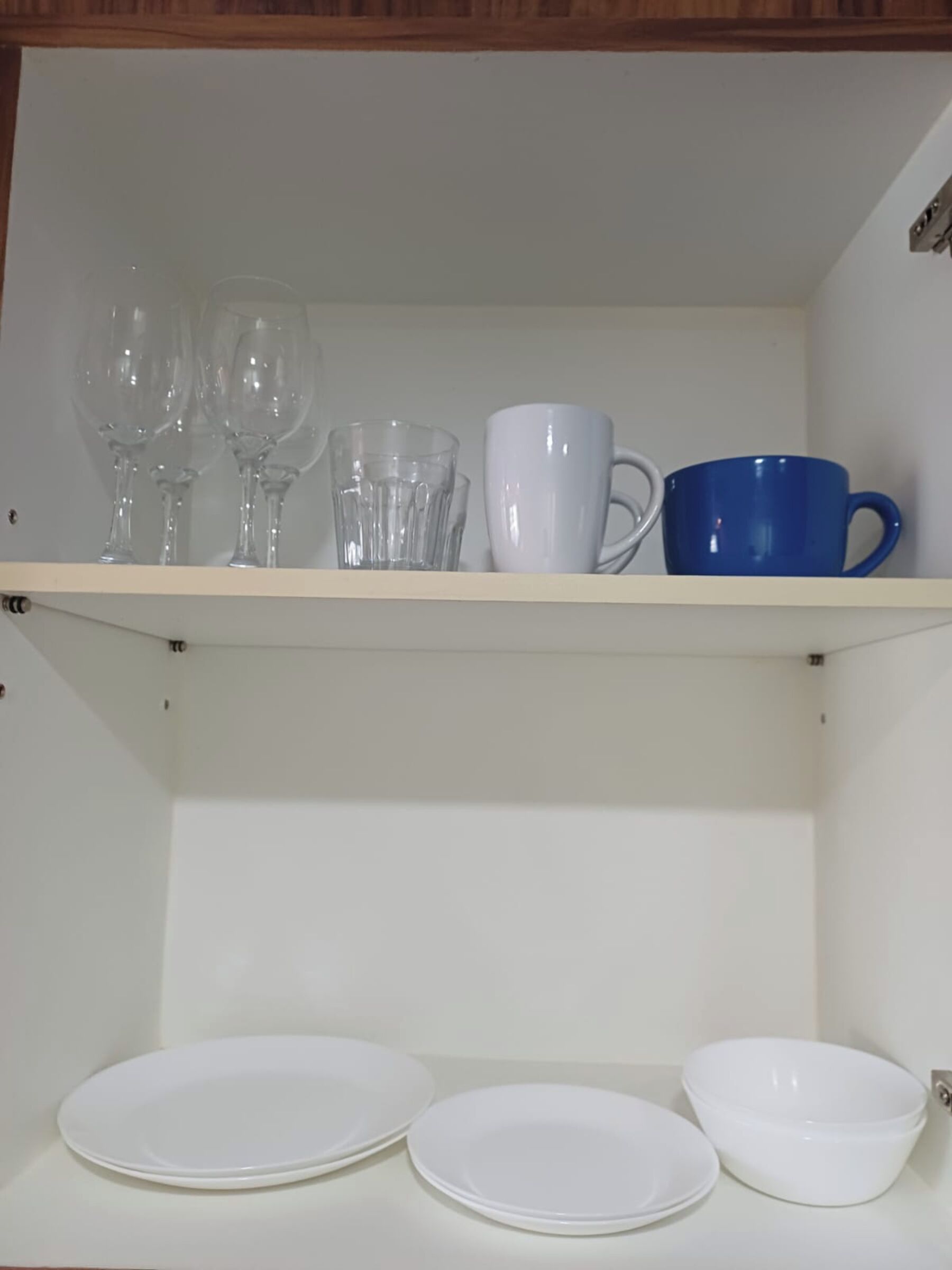 Uno scaffale con calici da vino, una tazza bianca e una tazza blu. In basso, piatti bianchi e una ciotola bianca.