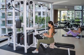 A gym with exercise equipment, a person using a machine, and another person doing floor exercises. - Dusit grand park I - Modern apartment all included - electricity water internet (Muang Pattaya)
