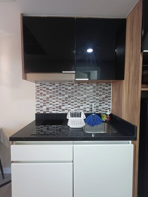 Une cuisine avec des meubles de couleur noire, un pare-feu en carreaux, un plan de travail noir et un appareil électroménager blanc placé en dessous.