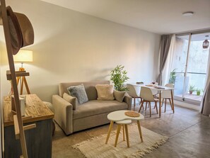 A living room with a sofa, a small table, a lamp, and a dining area with chairs and a table. - Cozy Apt with BBQ Balcony & Pool in Palermo Hollywood (Buenos Aires)