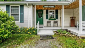 A small building with a porch labeled 'GUEST ROOMS,' two chairs, a green door, and a wooden bench.