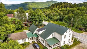 A two-story house with a green roof, a covered porch, and a driveway with a parked car.