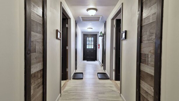 A hotel hallway with a light wood floor, dark wood paneling on the walls, a black door at the end, and a fire extinguisher mounted on the wall.