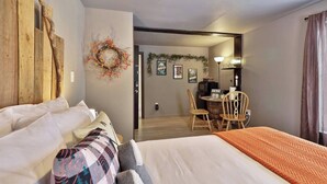 A bedroom with a bed, a desk with chairs, a television, and a wall with a wreath.