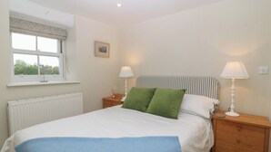 A bedroom with a bed, two bedside lamps, a radiator, a window with a curtain, and a picture on the wall.