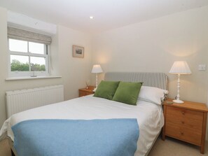 A bedroom with a bed, two bedside lamps, a radiator, a window with a curtain, and a picture on the wall. - THE BYRE, pet friendly, character holiday cottage in Tal-Y-Bont (Conwy)